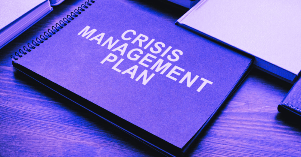 A close up of a black folder labelled Crisis Management Plan with a purple filter applied.