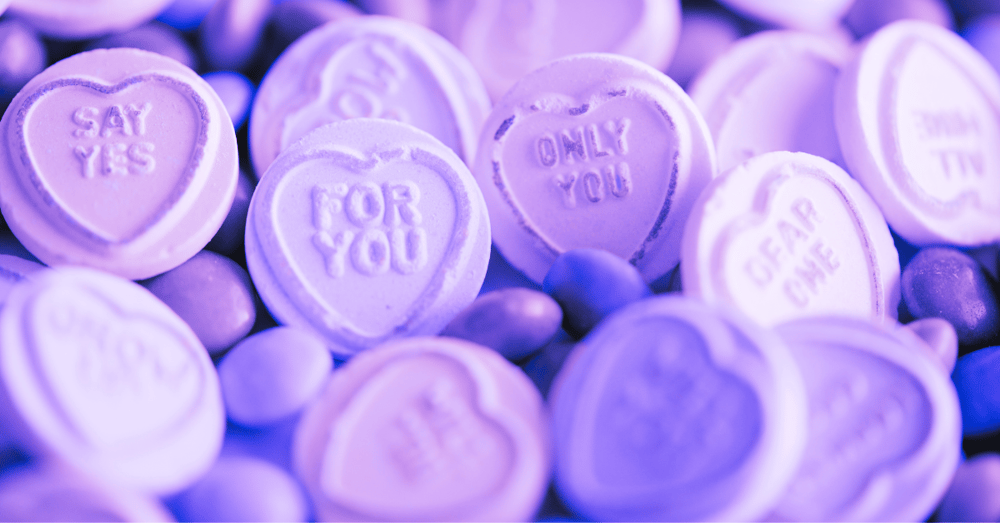 A close up of heart-shaped candies with words on them with a purple filter applied
