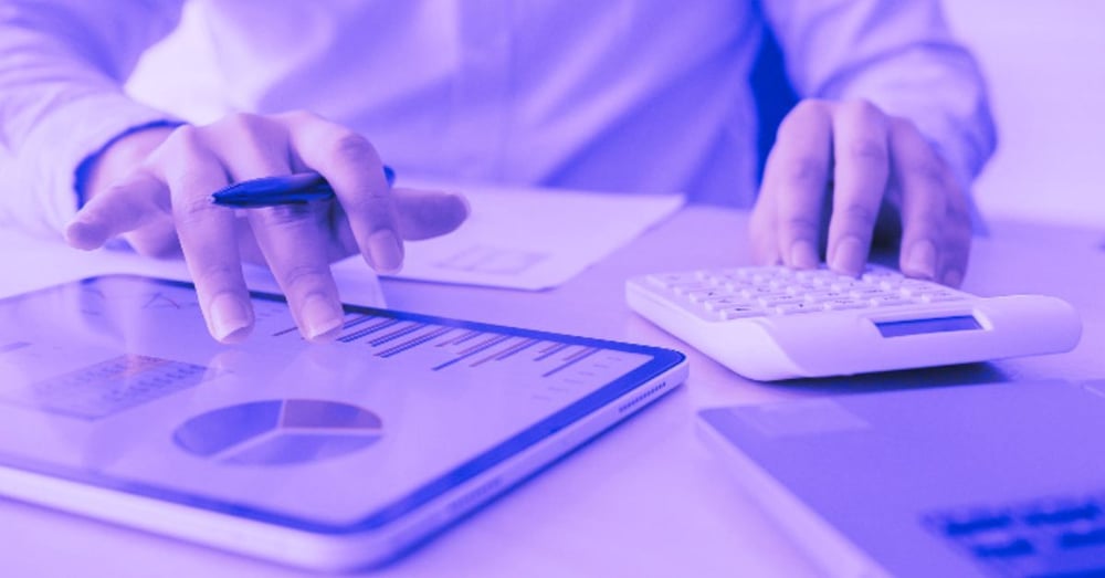 A person using a calculator while referring to charts on a tablet device.