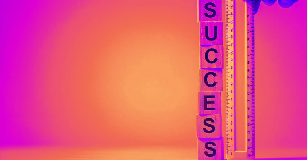 A measuring tape is held beside a stack of cubes which read 'success'.